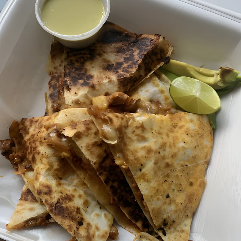 La Sureña Taquerias' quesadillas with a side of green sauce, lime, and avocado in a white container.