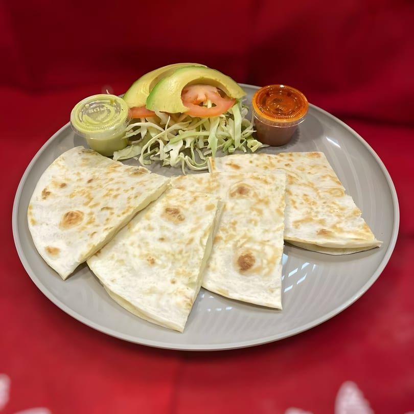 Four quesadilla slices with a side of shredded cabbage, avocado, tomato, and two dipping sauces.