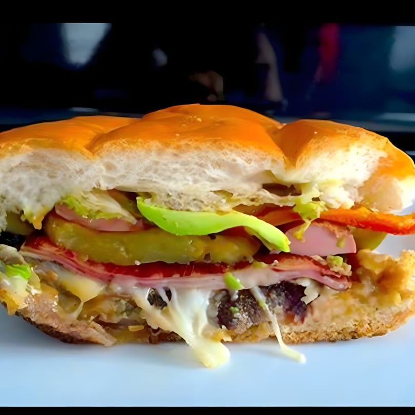 Close-up of a Mexican torta sandwich with melted cheese, avocado, ham, and pickles.
