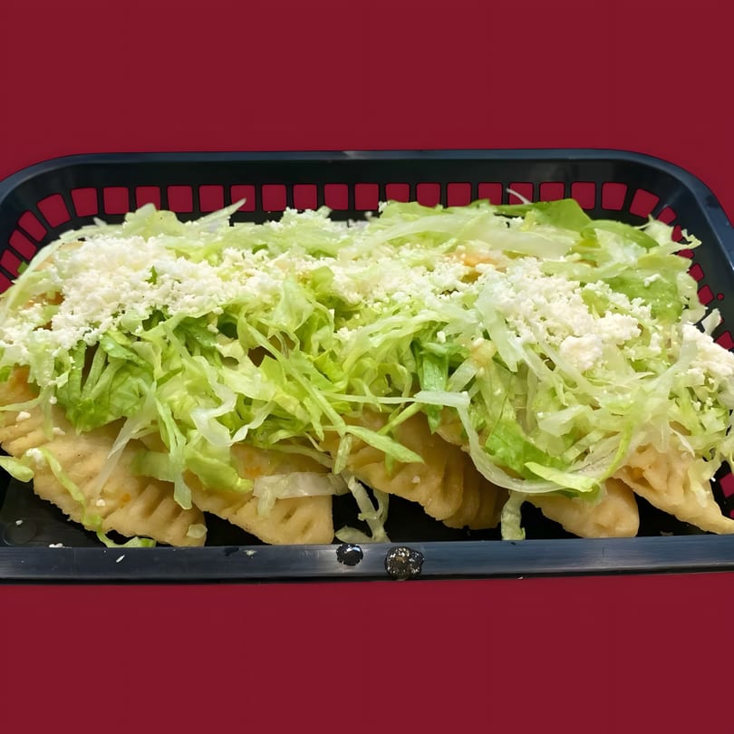 A black basket filled with golden-fried La Sureña Taquerias empanadas, topped with shredded lettuce and crumbled white cheese.