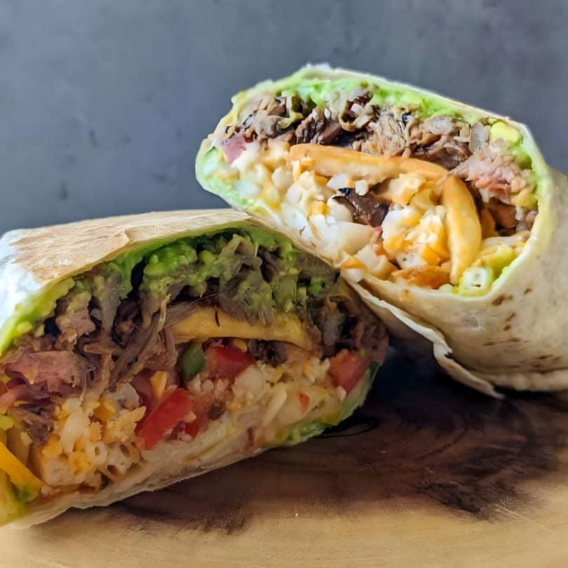 Two halves of a La Sureña Taquerias burrito, revealing meat, rice, guacamole, and vegetables.