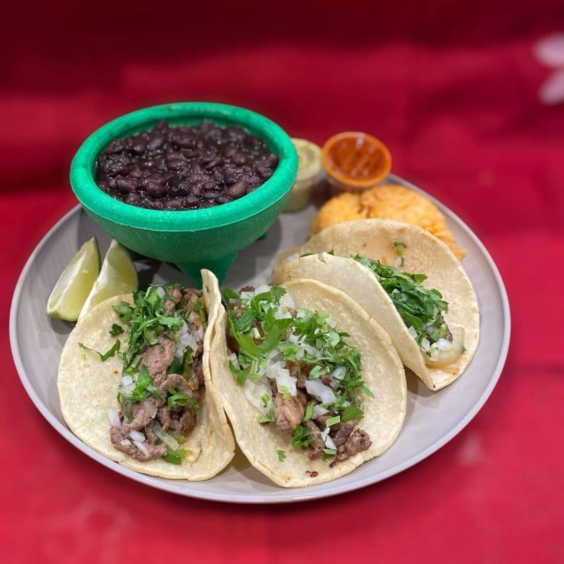 Three La Sureña Taquerias tacos with meat, onions, cilantro, lime, rice, beans, and salsa.